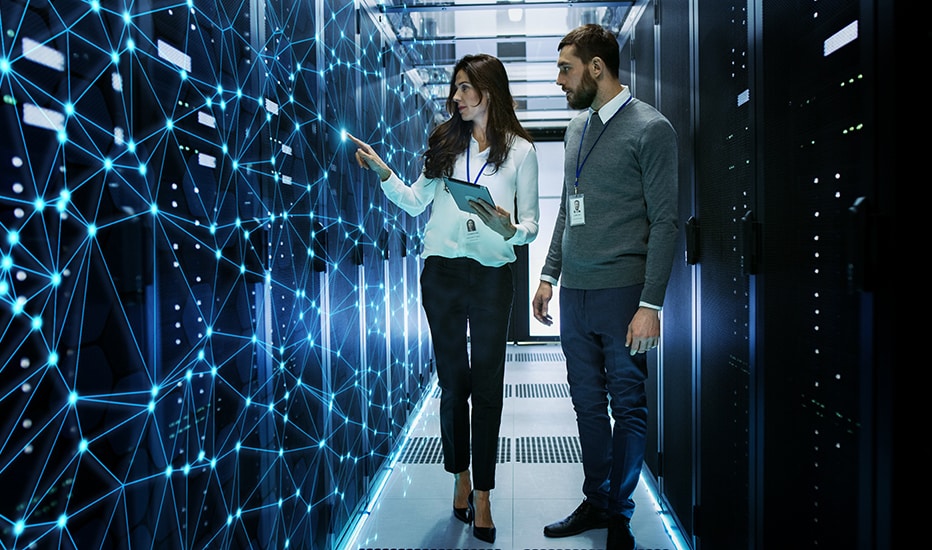 A female and male IT engineers discuss technical details while walking down a data center’s server rack corridor.
