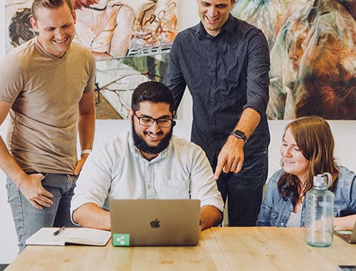A team of smiling creative agency employees work together on Apple MacBook Pro laptops.