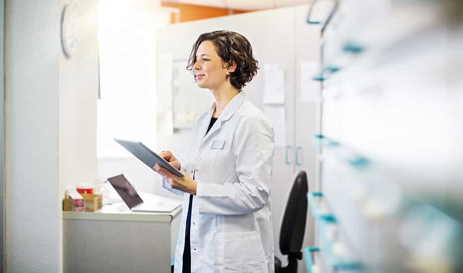 A smiling pharmacist enters patient information into her hospital issued tablet.