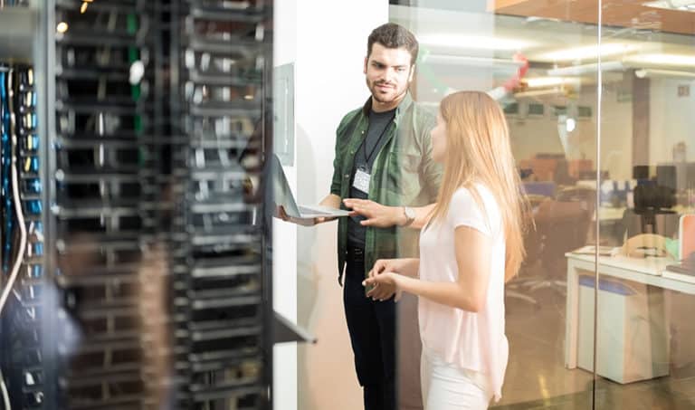 An IT manager consults with a colleague in a glass-walled server room.