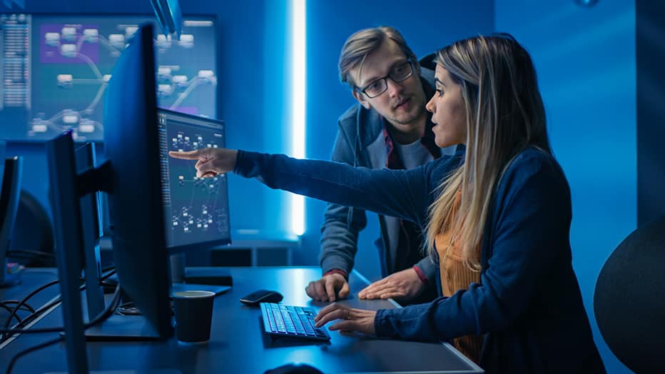 A male and female cybersecurity specialists located in their managed security services provider’s security operation center (SOC) are seen actively defending a network against a cyberattack.