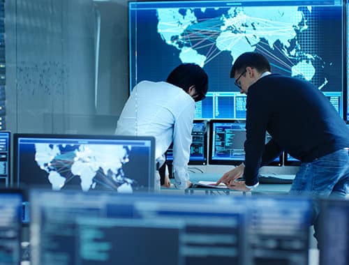 Two managed services security specialists review a network assessment within their SOC office.
