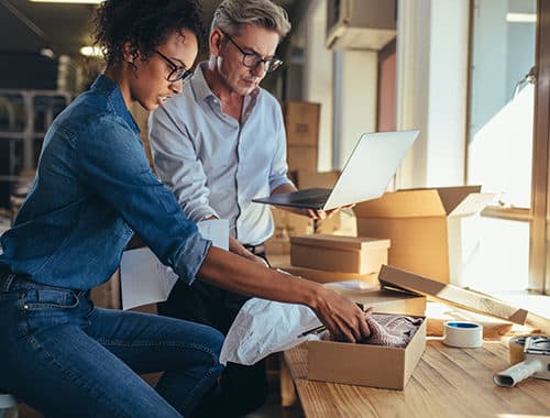 Two small business partners, an attractive African American woman and caucasian middle-aged man, ship and track inventory for their business using QuickBooks.