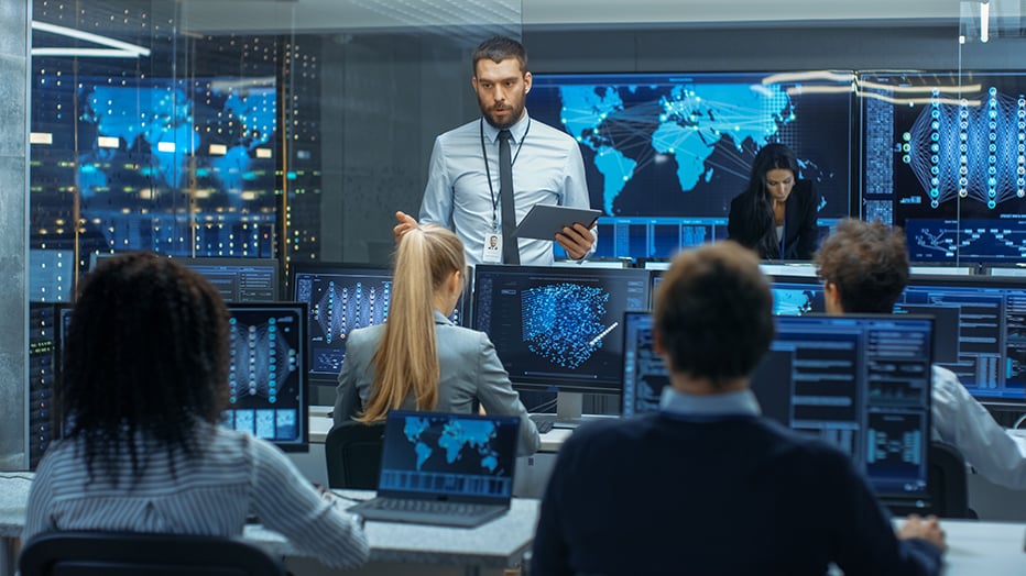A chief security officer located at the center of a SOC discusses project plans, including implementation and required remediation tactics, with his team of security professionals.