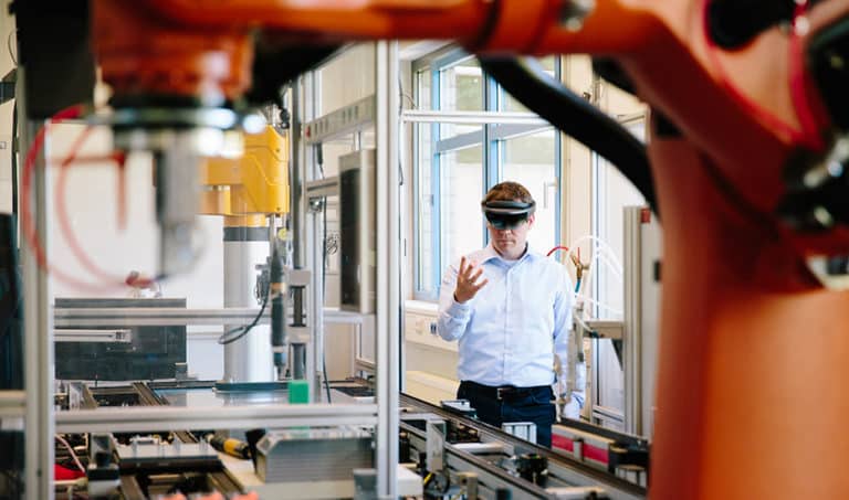 An engineer works with a HoloLens place a virtual robotic arm into the production line as manufacturing companies embrace industry 4.0.