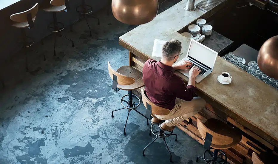 A high-angle shot of a businessman writing an email in Microsoft Outlook on his laptop at the counter of a cafe.