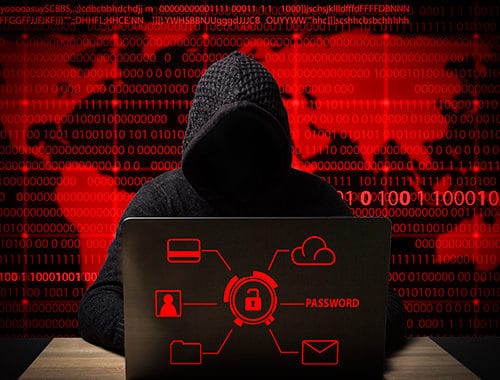 A hacker in a black hoodie sits a desk in front of a laptop attempting to compromise a small business network. Binary code overlays a global map in the background.