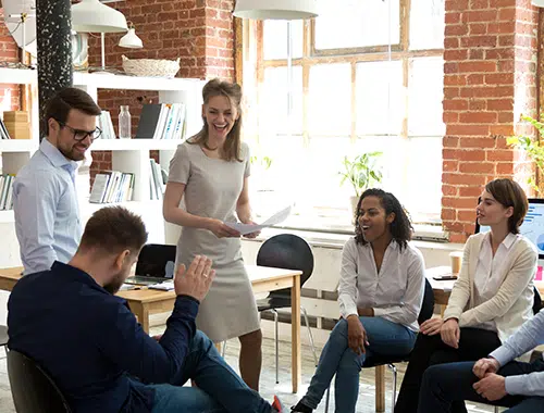 A diverse team of seven employees participate in an engaging company brief meeting, colleagues are joking with each other and enjoying the open and transparent communication