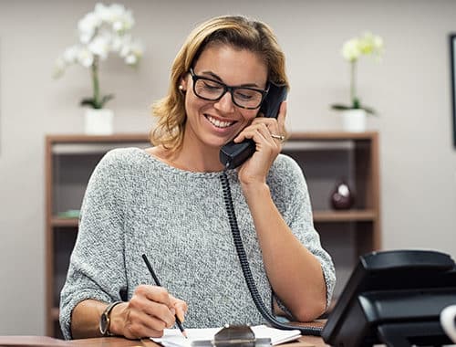 Beautiful mature business woman speaking on a Polycom Voice over Internet Protocol business desk phone at a creative agency office.  