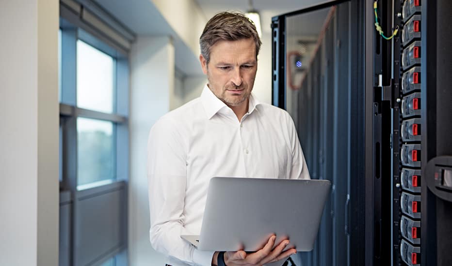 A confident, smiling male IT server technician checks a server located in a server room.