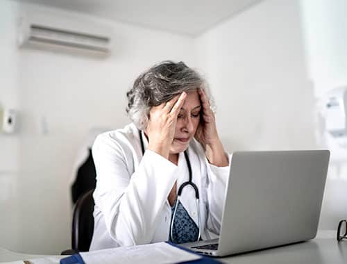 A worried and tired looking doctor appears concerned while using her laptop.