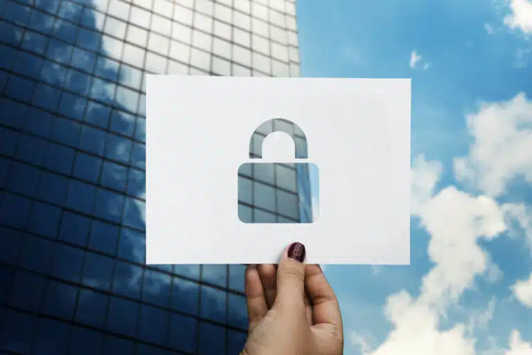 A person holding a piece of paper with a padlock shape cut out, in front of an office building with clouds to the right - a symbol of SSO in the Cloud.