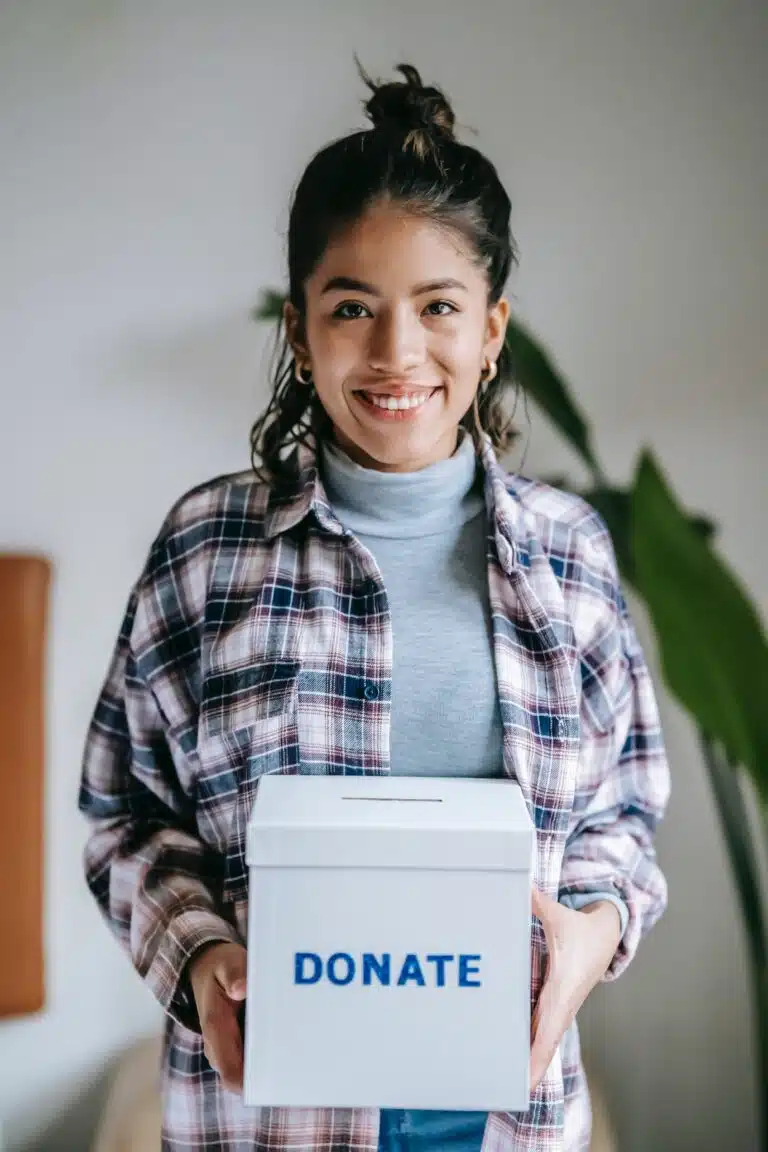 Woman with plaid shirt with hair up holding a white donation box.